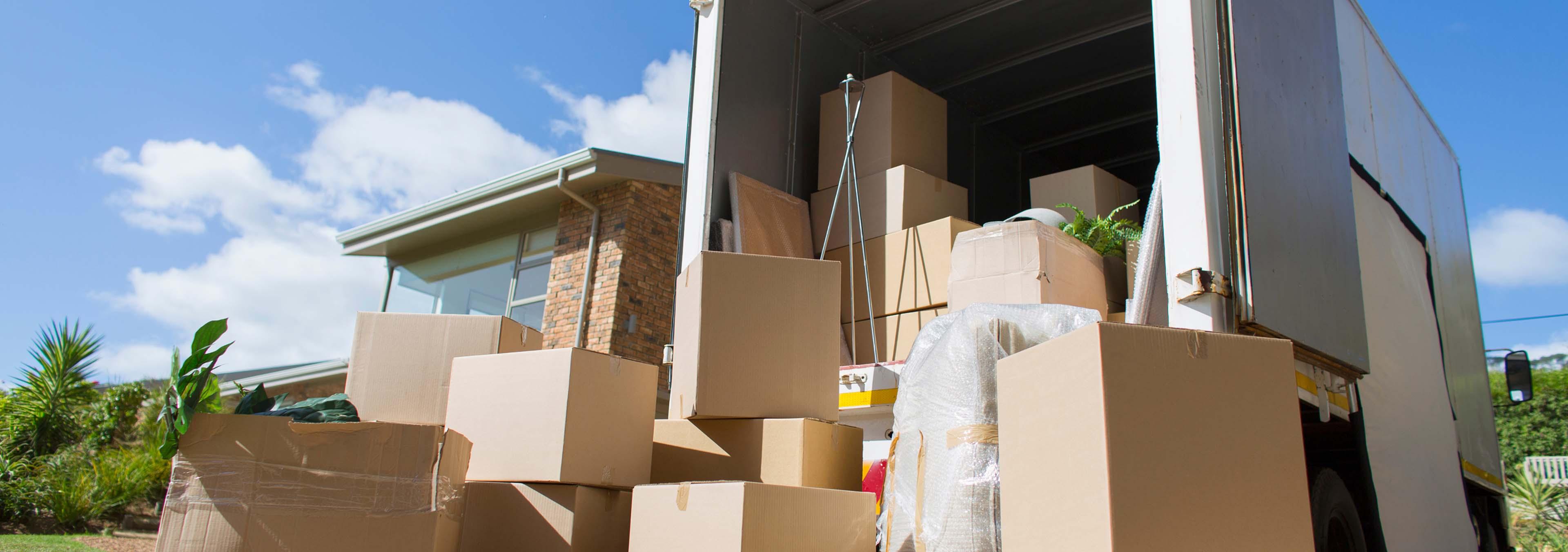Van parked in front of a house with boxes inside and stacked outside.