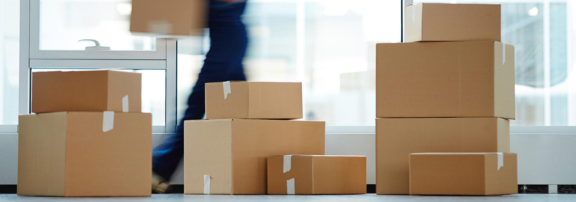 Stacked moving boxes in a bright room with a person walking by, representing an International Van Lines move.
