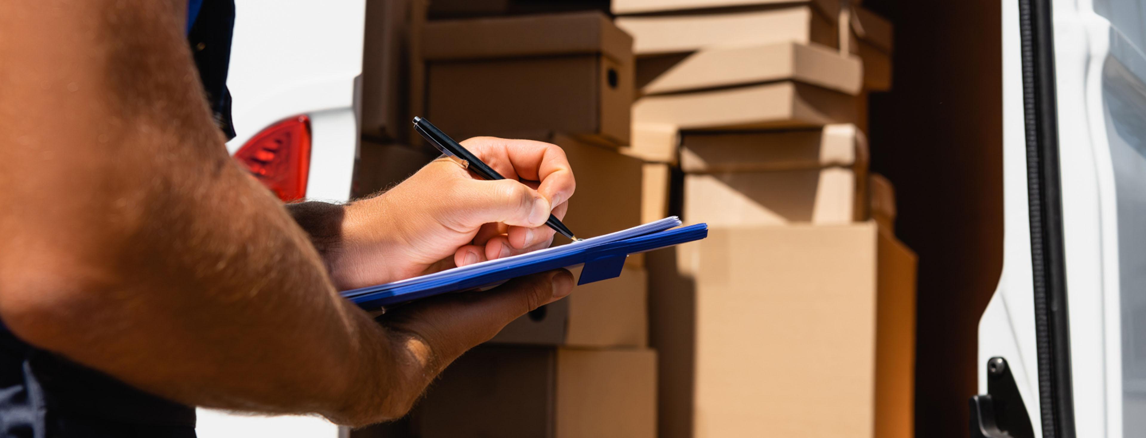 Person holding clipboard and pen near packed boxes, managing paperwork for an International Van Lines move.