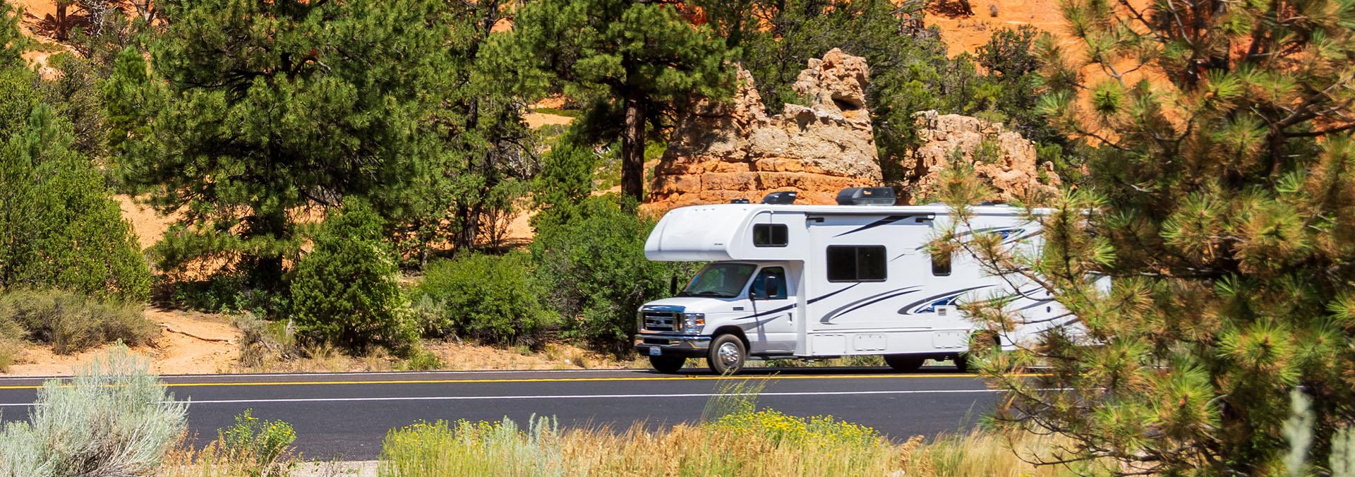 RV driving on a road surrounded by trees and rocks.